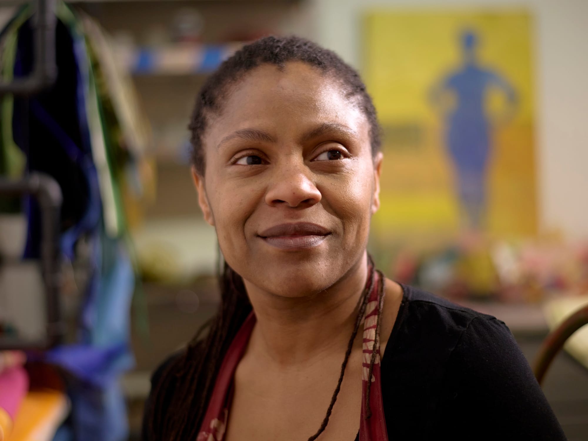 A woman from the shoulders up, the strap of an apron visible, looking to the side and smiling