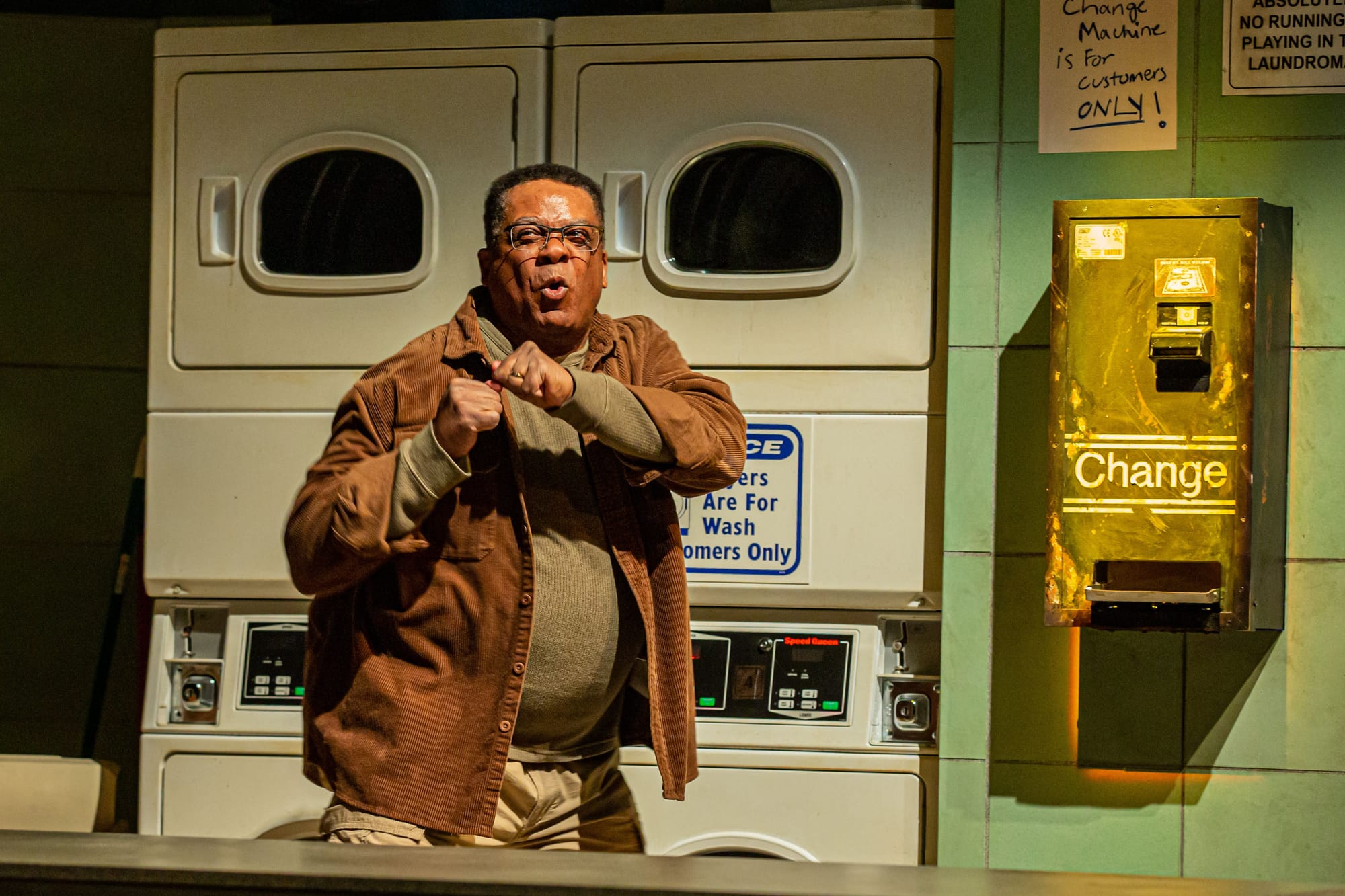 A man shadowboxes in an onstage laundromat