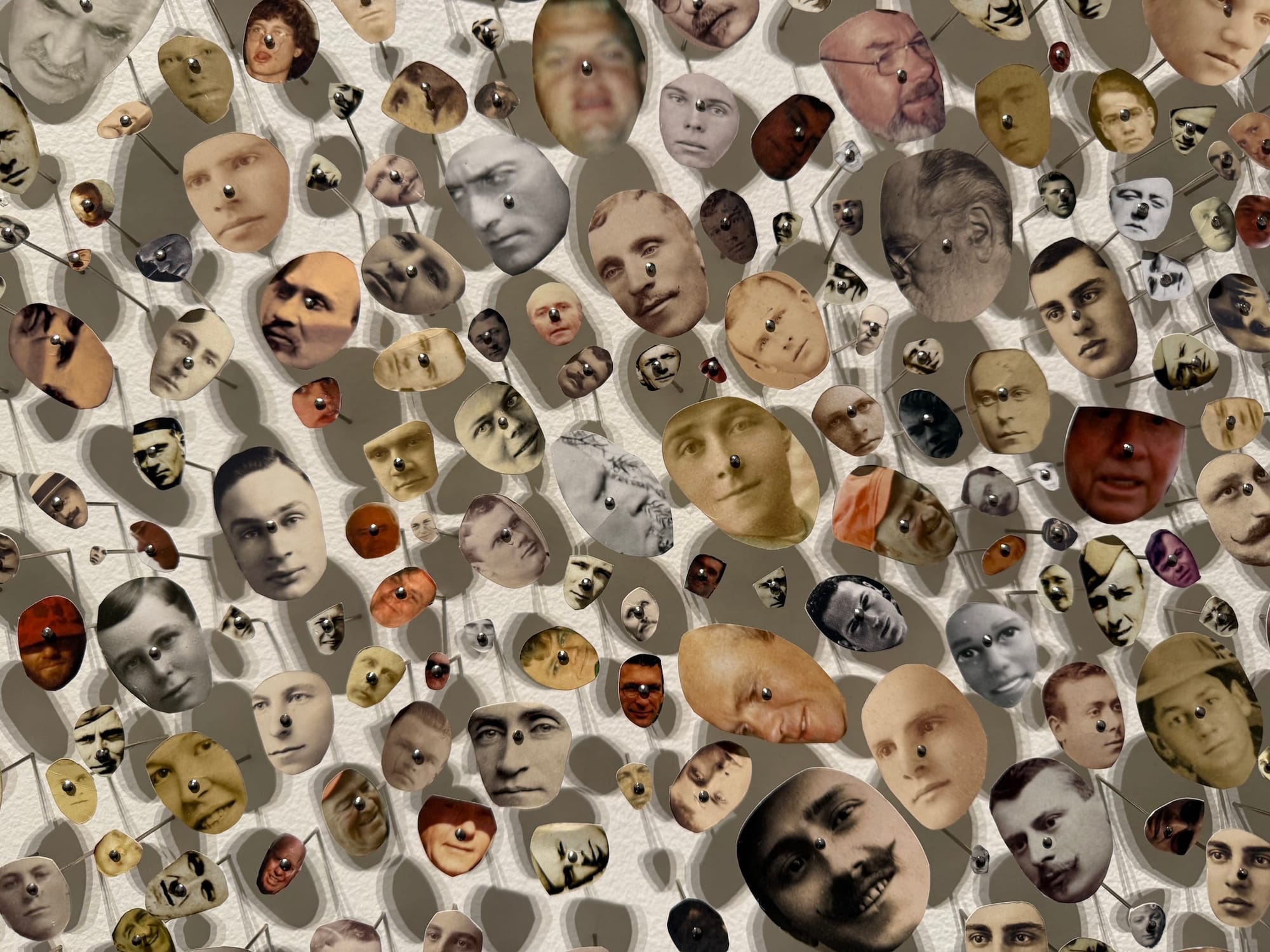Tons of tiny heads, cut from old photos, are pinned individually to a wall