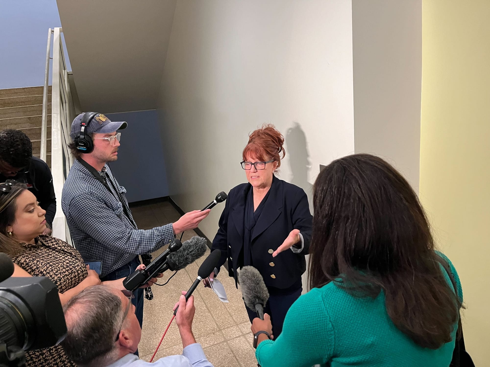 a red haired woman is surrounded by reporters in a white hallway