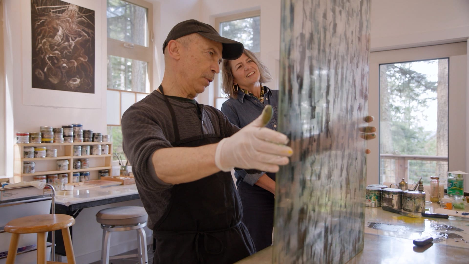 A man and woman in an art studio look at an abstract painting on a piece of plexiglass. (Art by Northwest / Cascade PBS)