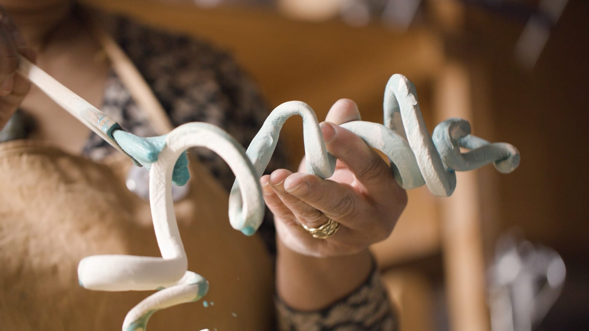 Close-up of a hand holding a clay squiggle that's being painted with blue glaze
