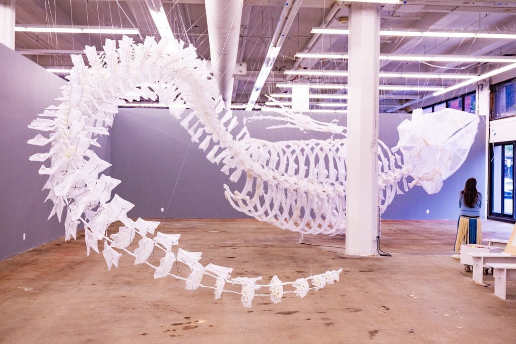 Photo of a huge suspended sculpture of a white whale skeleton.