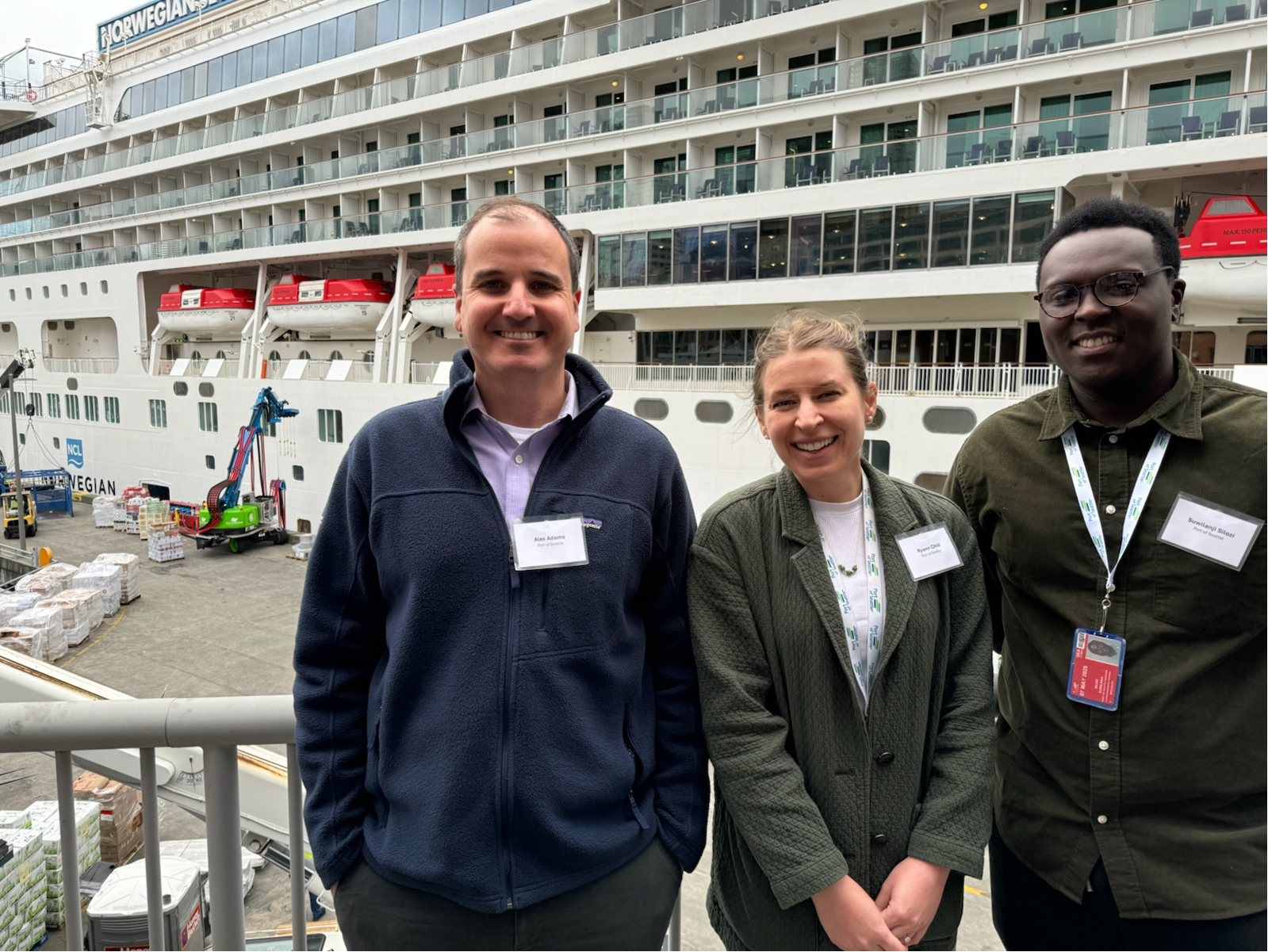 Three people smile in front of a Norwegian cruise