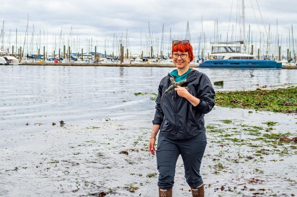 Jenn Stebbing holds a starfish off the coast with ships in the background