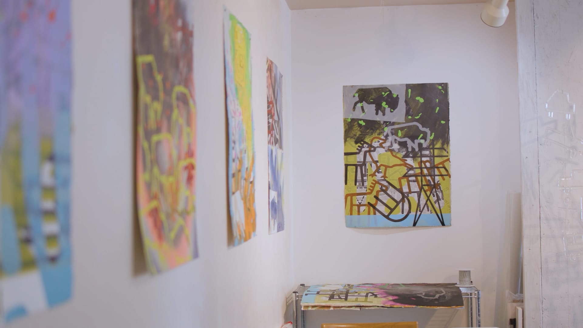 Photo of a wall hung with multiple, multicolored abstract prints featuring images of buffalo and other symbols.