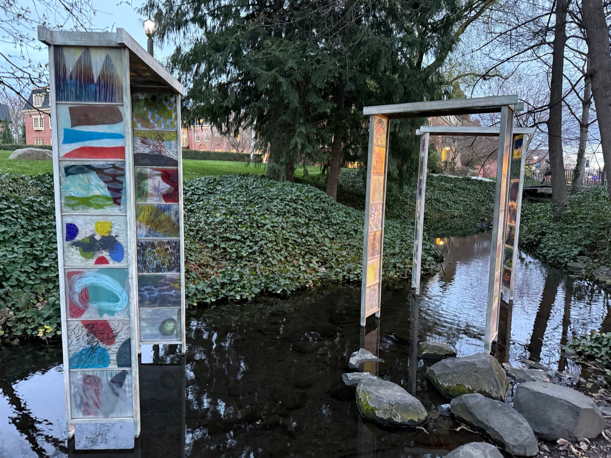 A creek in which three tall angular gates appear midstream. Each has glass panels containing abstract shapes and colors.