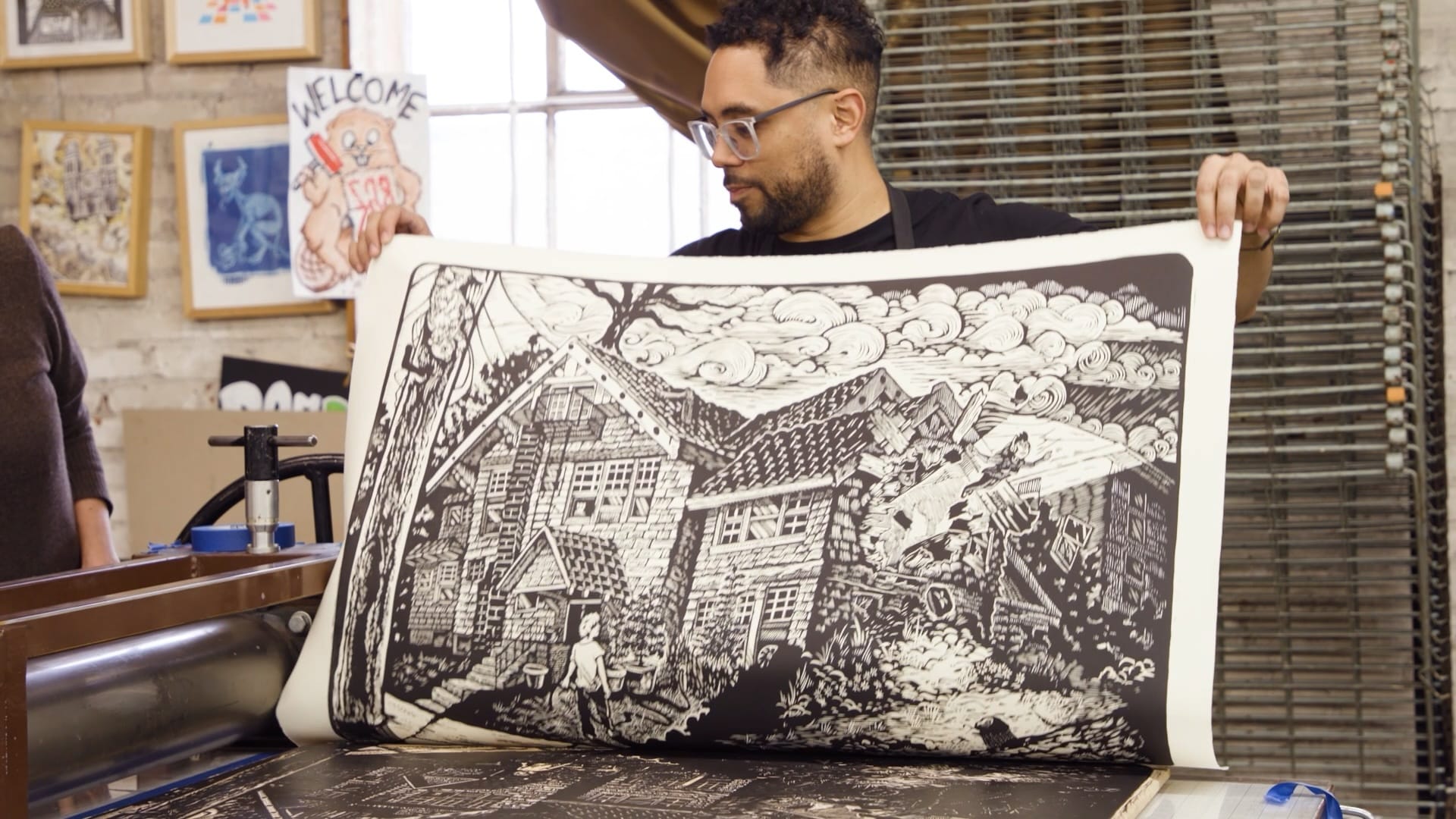A man with glasses holds up a print of a NW home, just coming off a press.