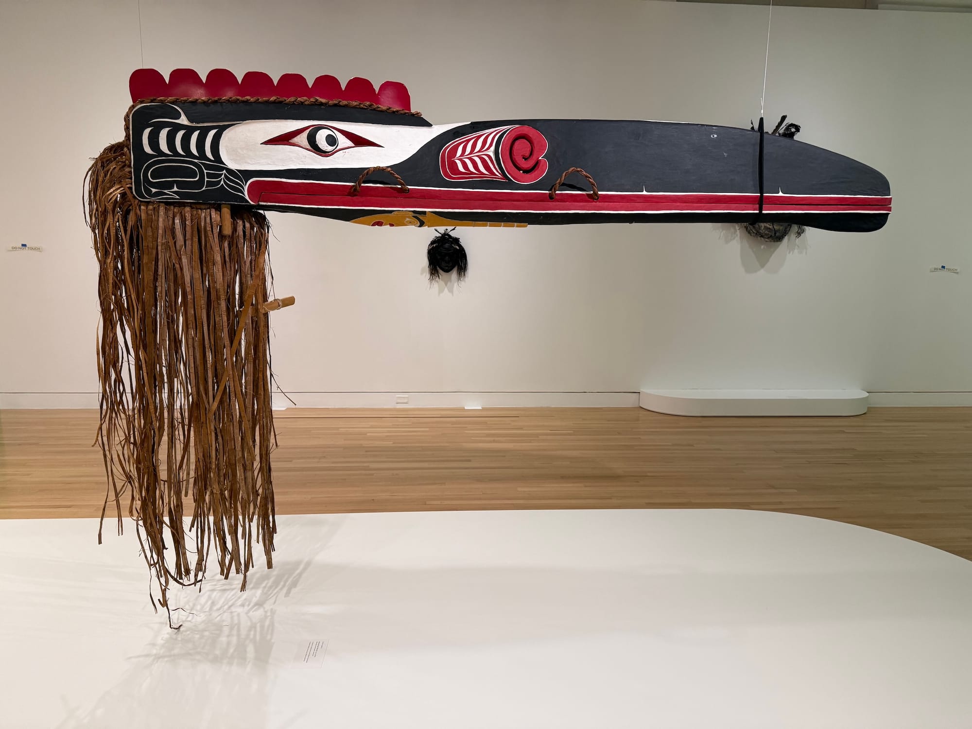 Photo of an Indigenous raven mask with long hair and a very long, skinny beak tied closed with string.