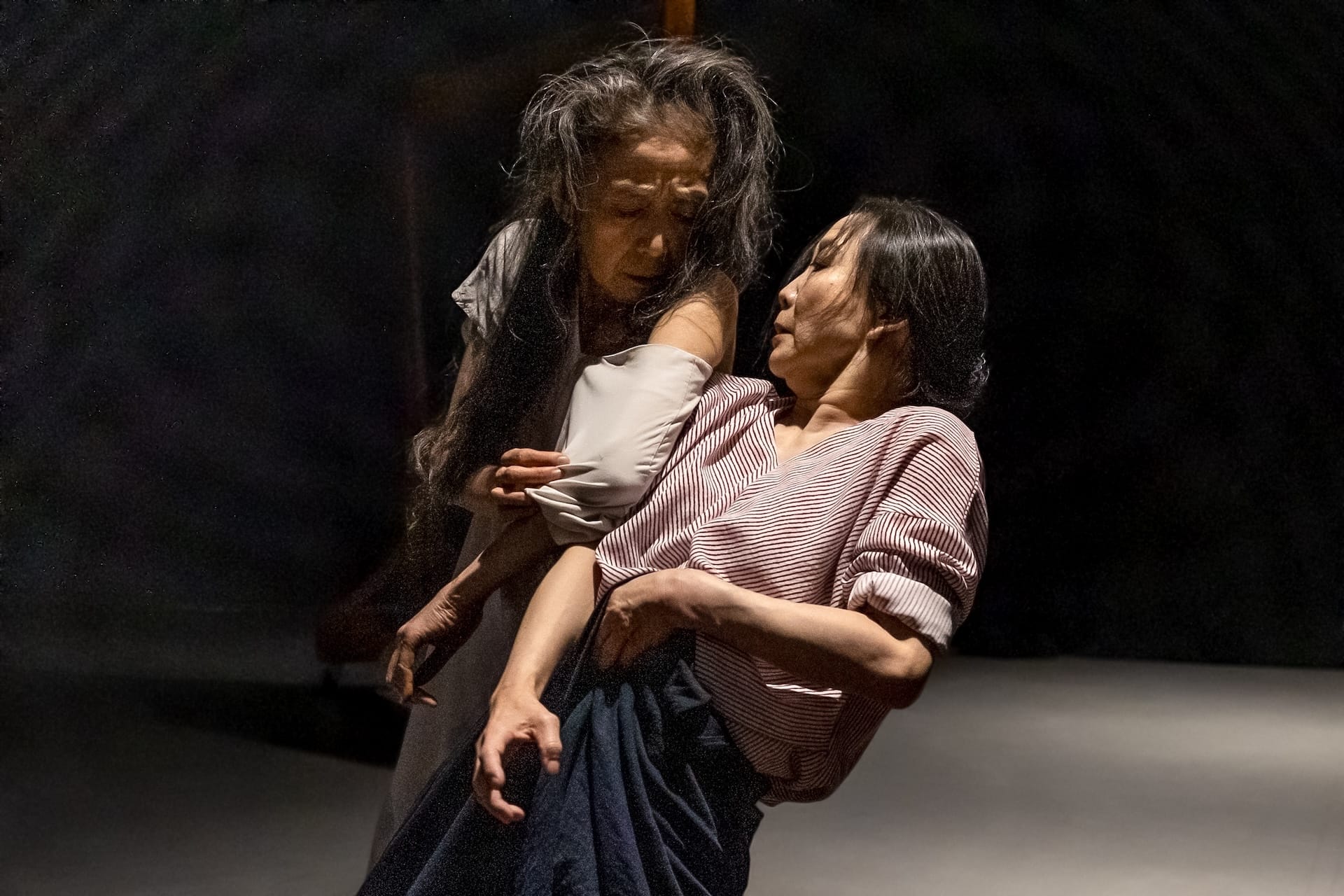 Two women dancers with long black hair push together in an anxious pose.