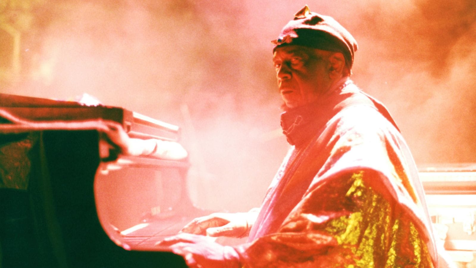 A film still of a person playing the piano, bathed in warm smoky orange lighting.