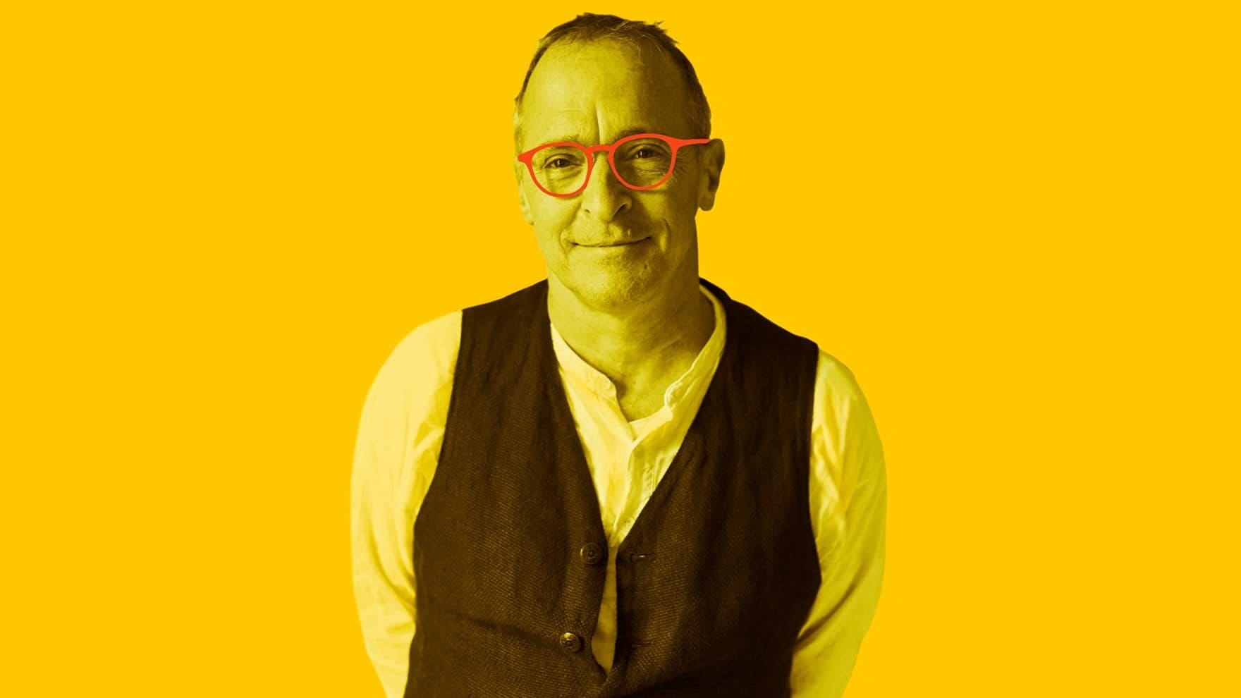 Photo of a smiling man with close-cropped hair wearing a white shirt, vest and glasses.