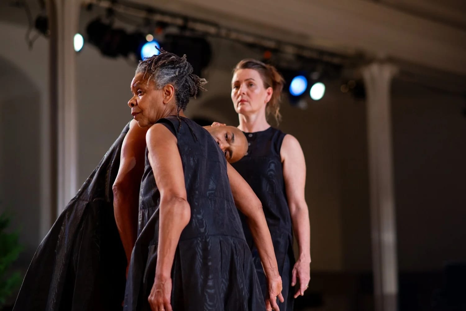 Three dancers in simple black shifts cluster together on stage