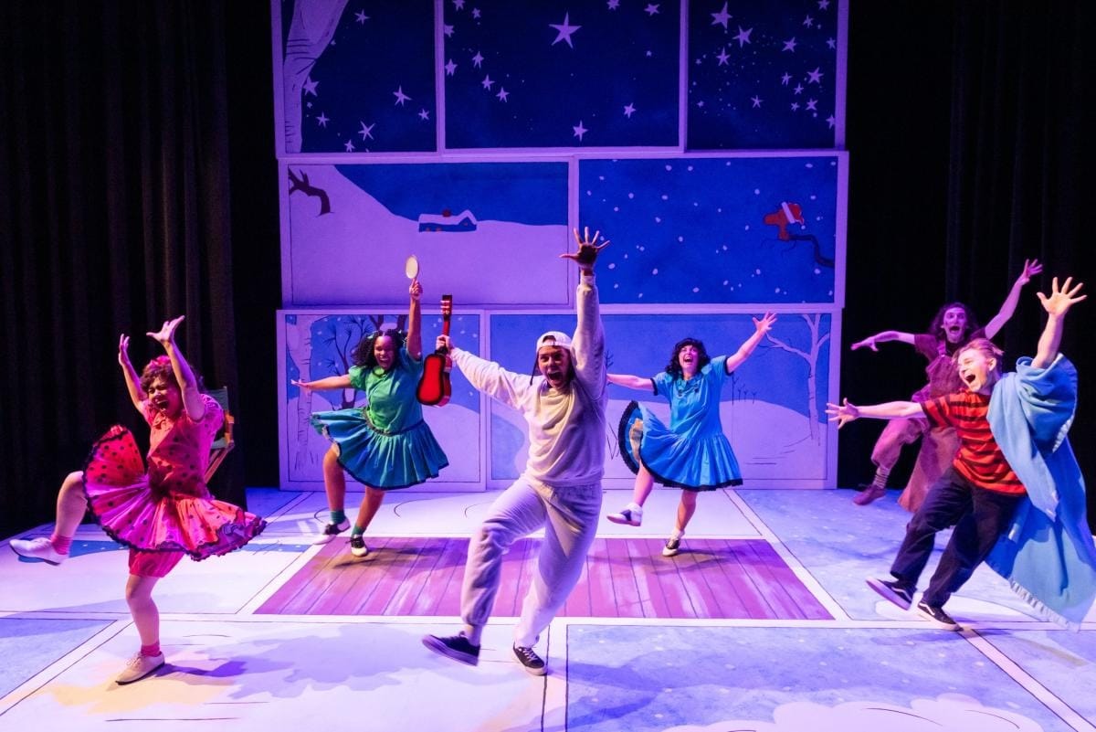 A stage production in which six performers in bright childlike costumes dance enthusiastically.
