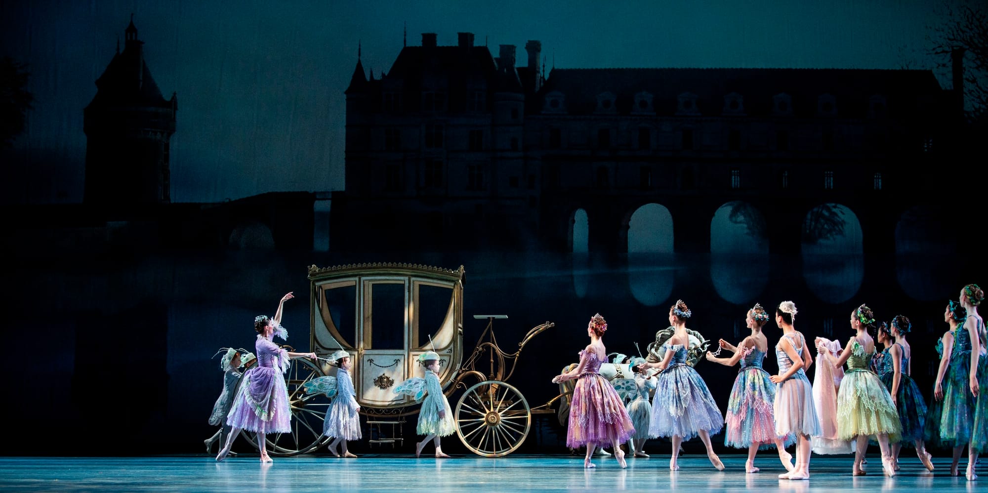 Photo of a stage production of Cinderella, with colorfully dressed ballerinas approaching a carriage. 