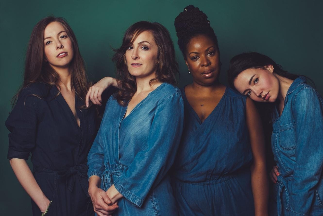 Four women dressed in shades of blue, all facing the camera.