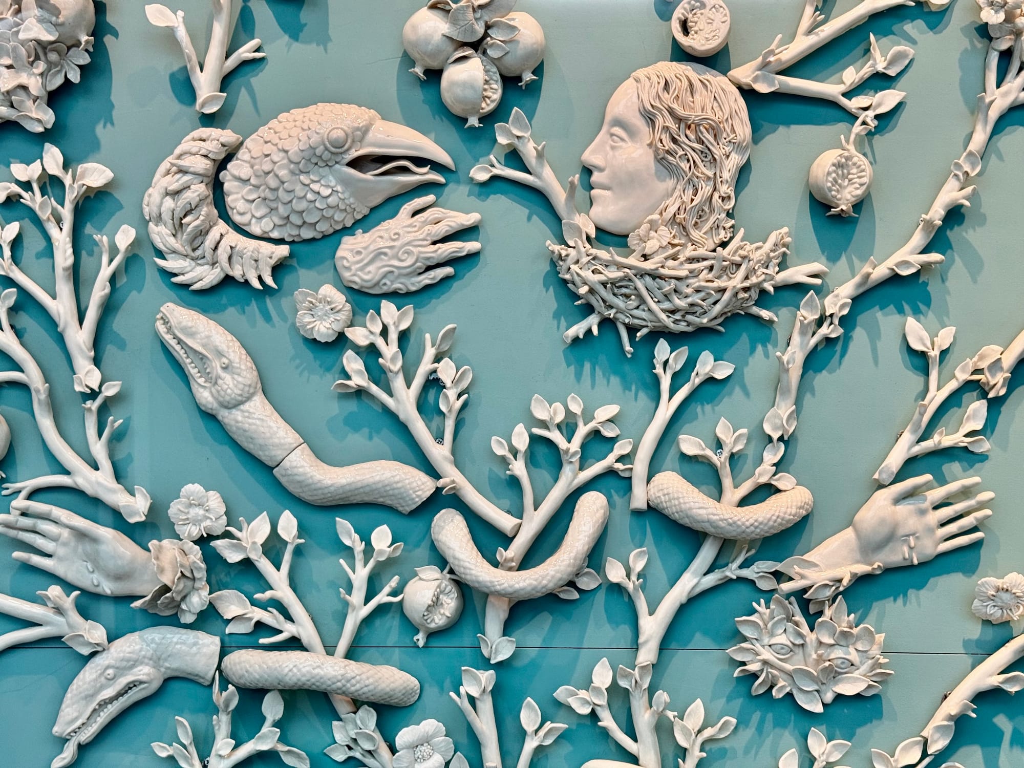 White ceramic wall sculpture made of many branching pieces including snakes, hands, branches and flowers
