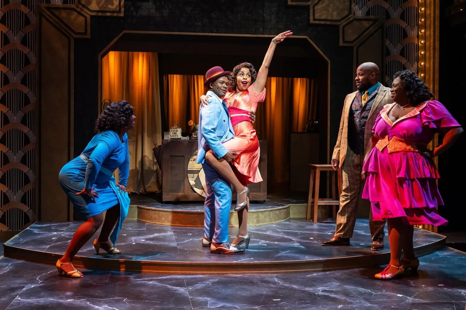 Photo of a stage performance in which three women and two men wear bright, shiny period costumes and dance