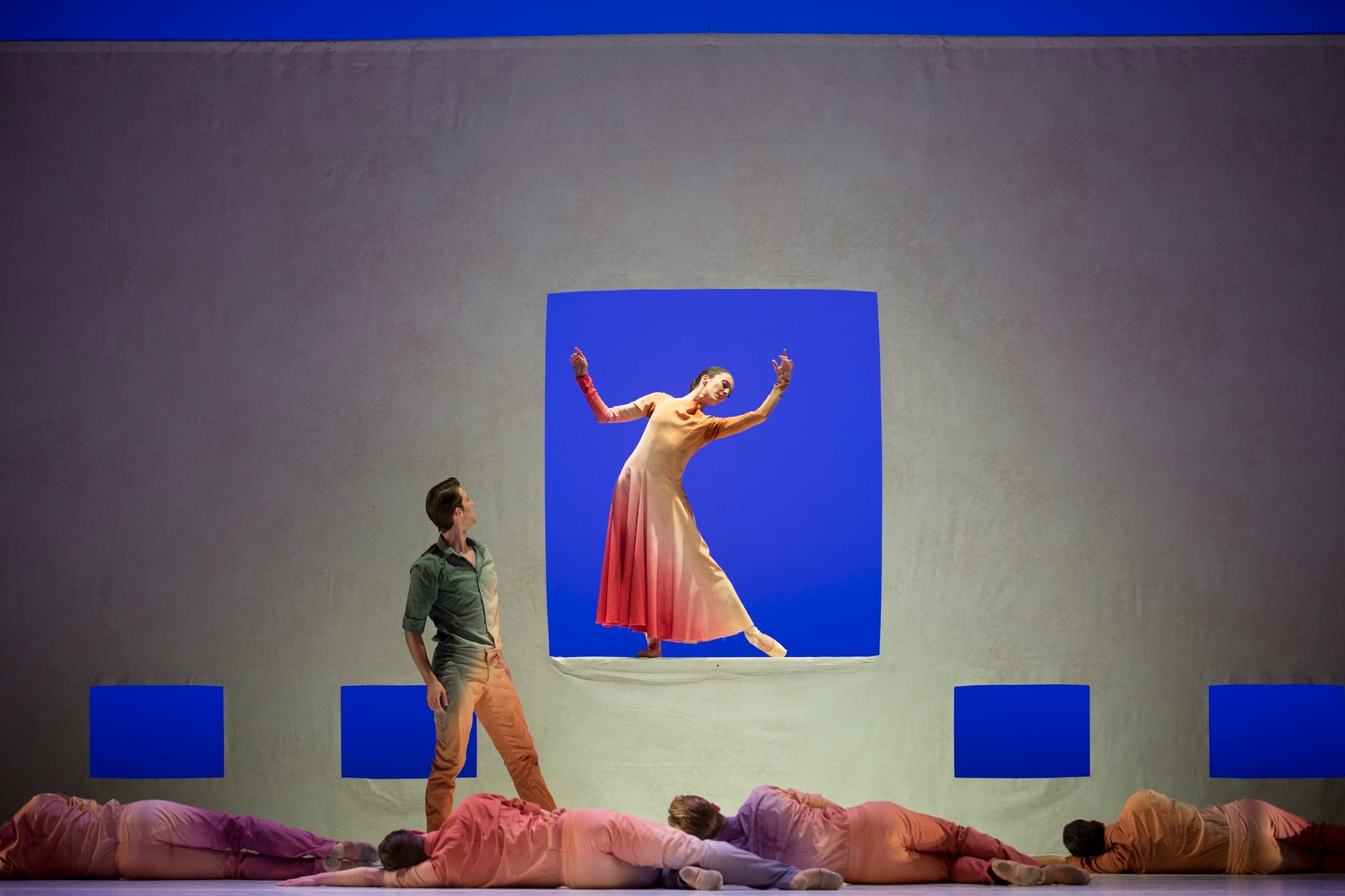 A photo of a ballet performance featuring a woman bent gracefully inside a blue square in a wall