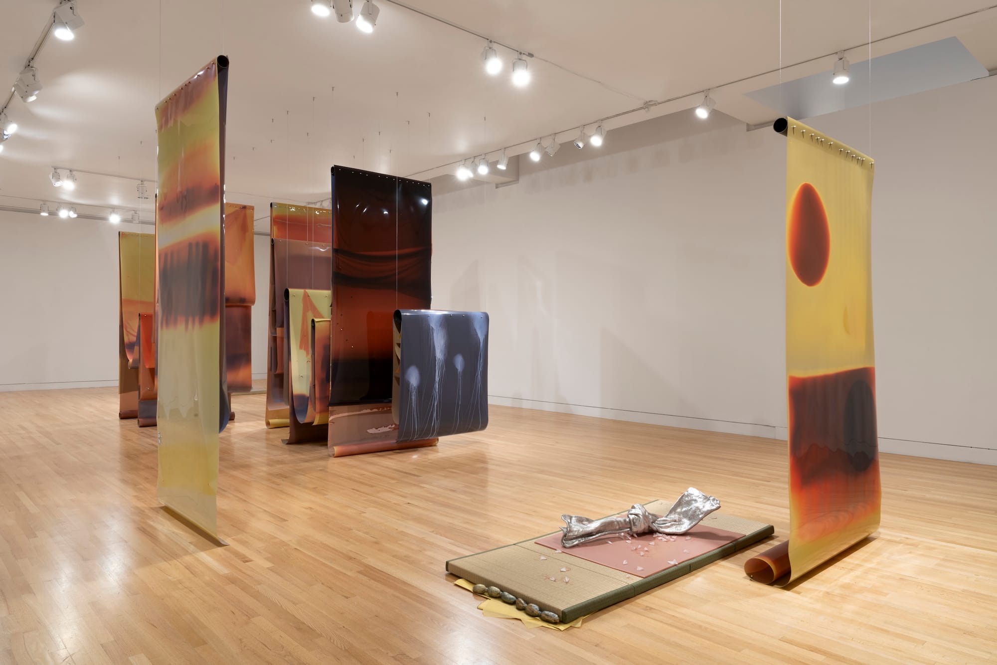 Long, thin colored scrolls hang from the ceiling in a white gallery room