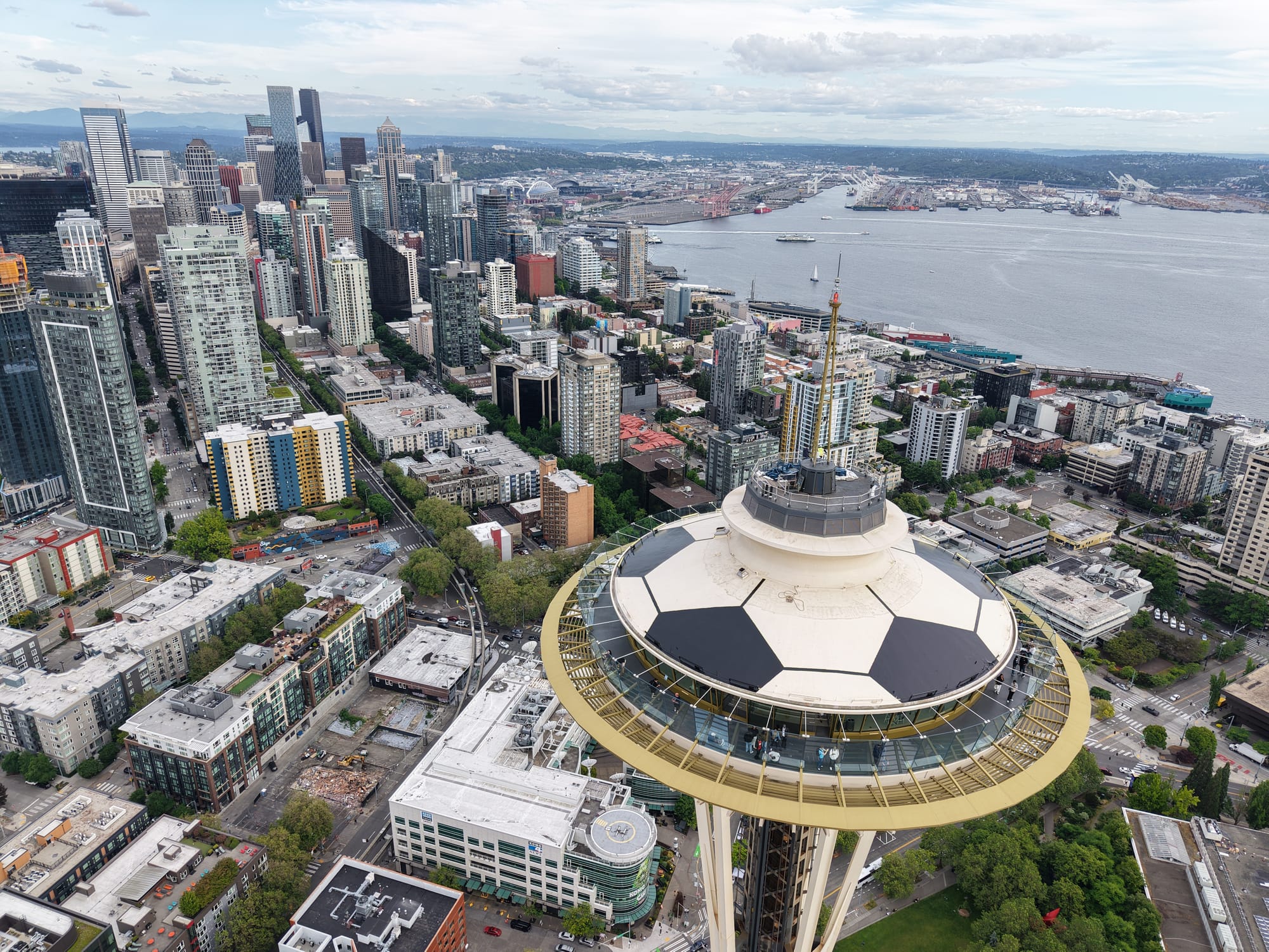 Drone photo of the top of the Space Needle, which has been painted like a soccer ball, with Seattle skyline behind