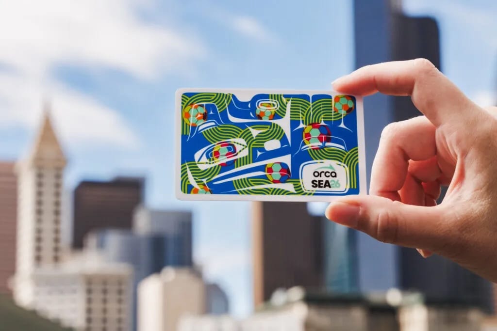 photo of a hand holding up a metro card with Native designs including raven heads and whale tails, plus soccer balls