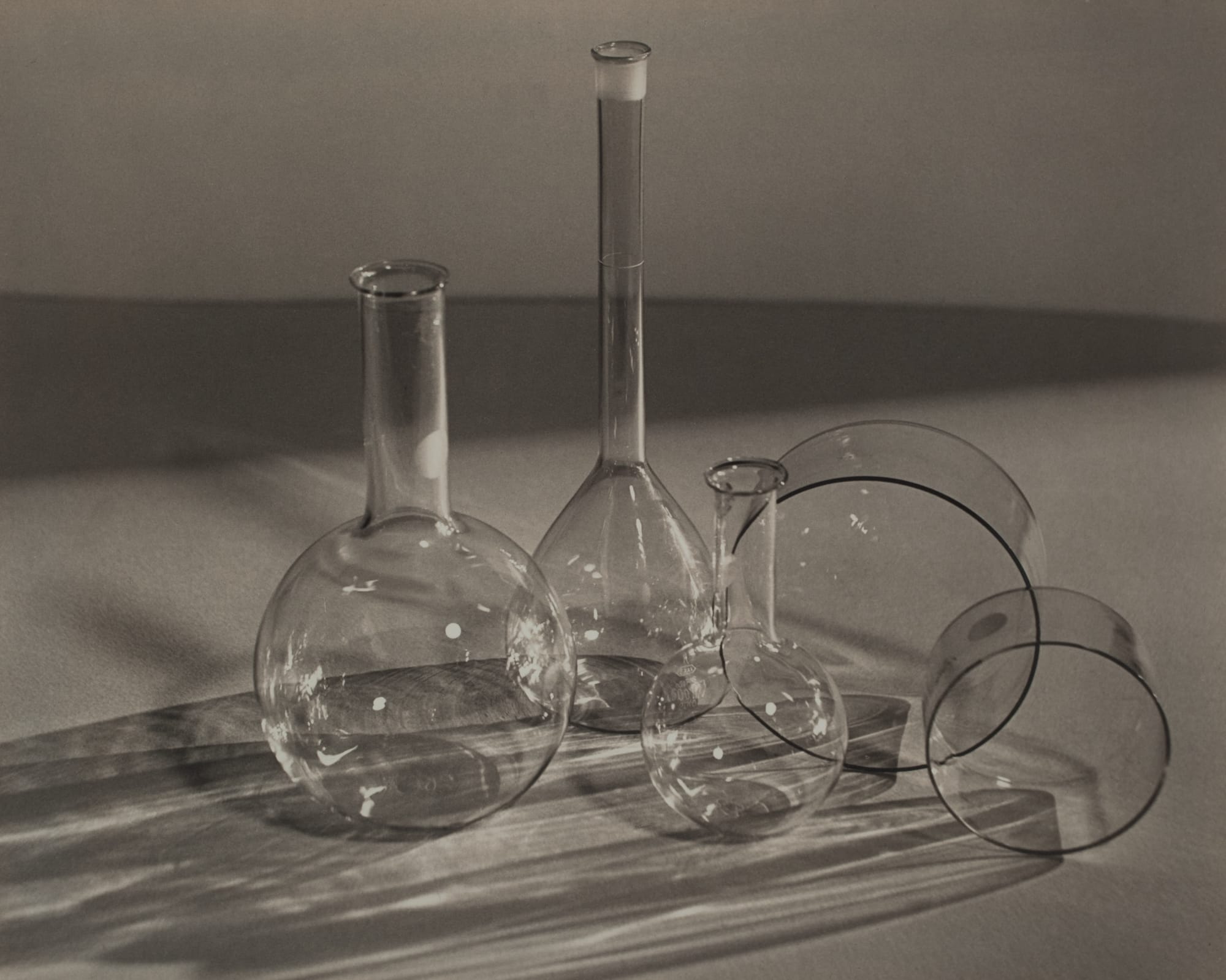 A vintage black and white photo of glass beakers casting shadows on a table