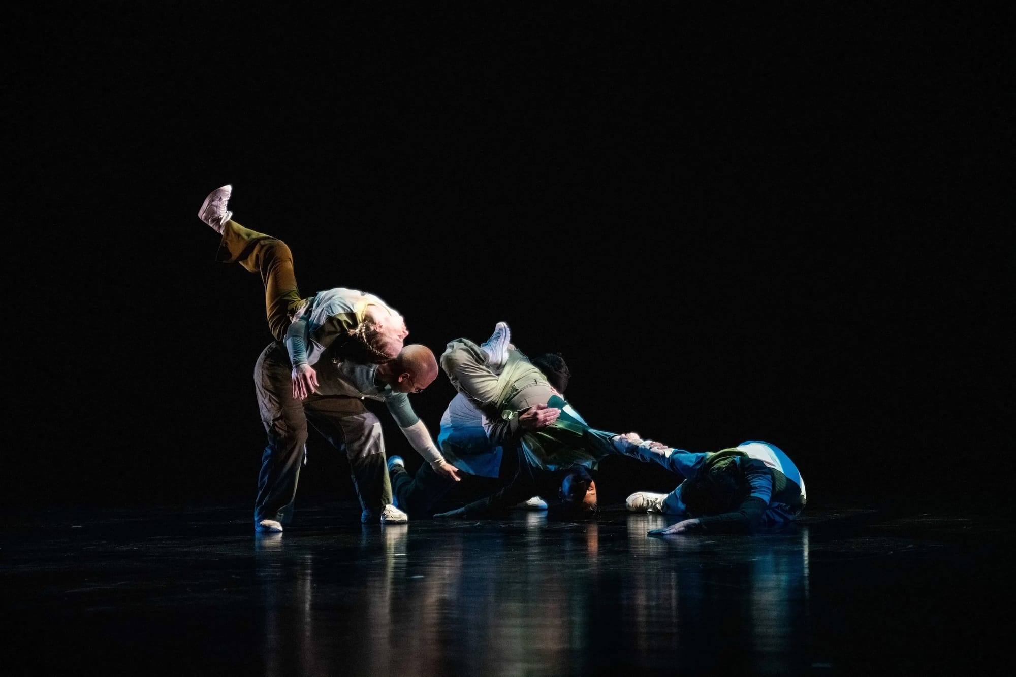 Three dancers contorted together on darkened stage