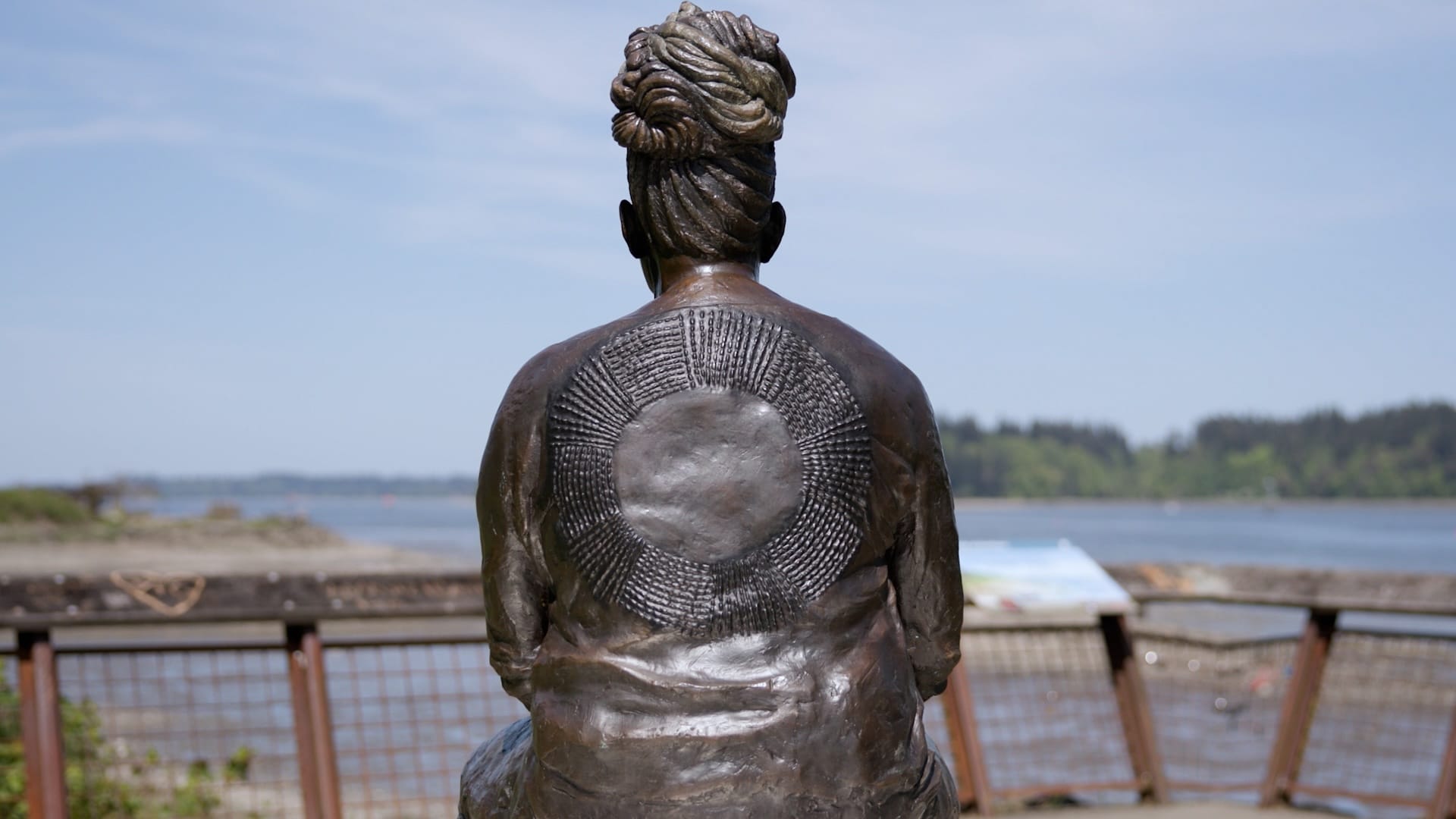 A bronze sculpture of a woman with braids piled on her head, looking out to the sea.