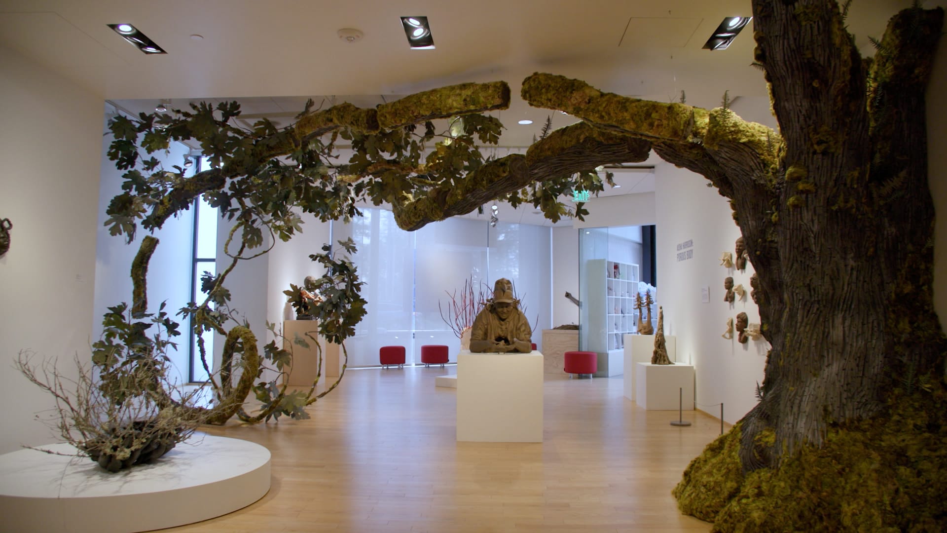 An art gallery installation of clay busts, dominated by a giant tree branching over the other art.