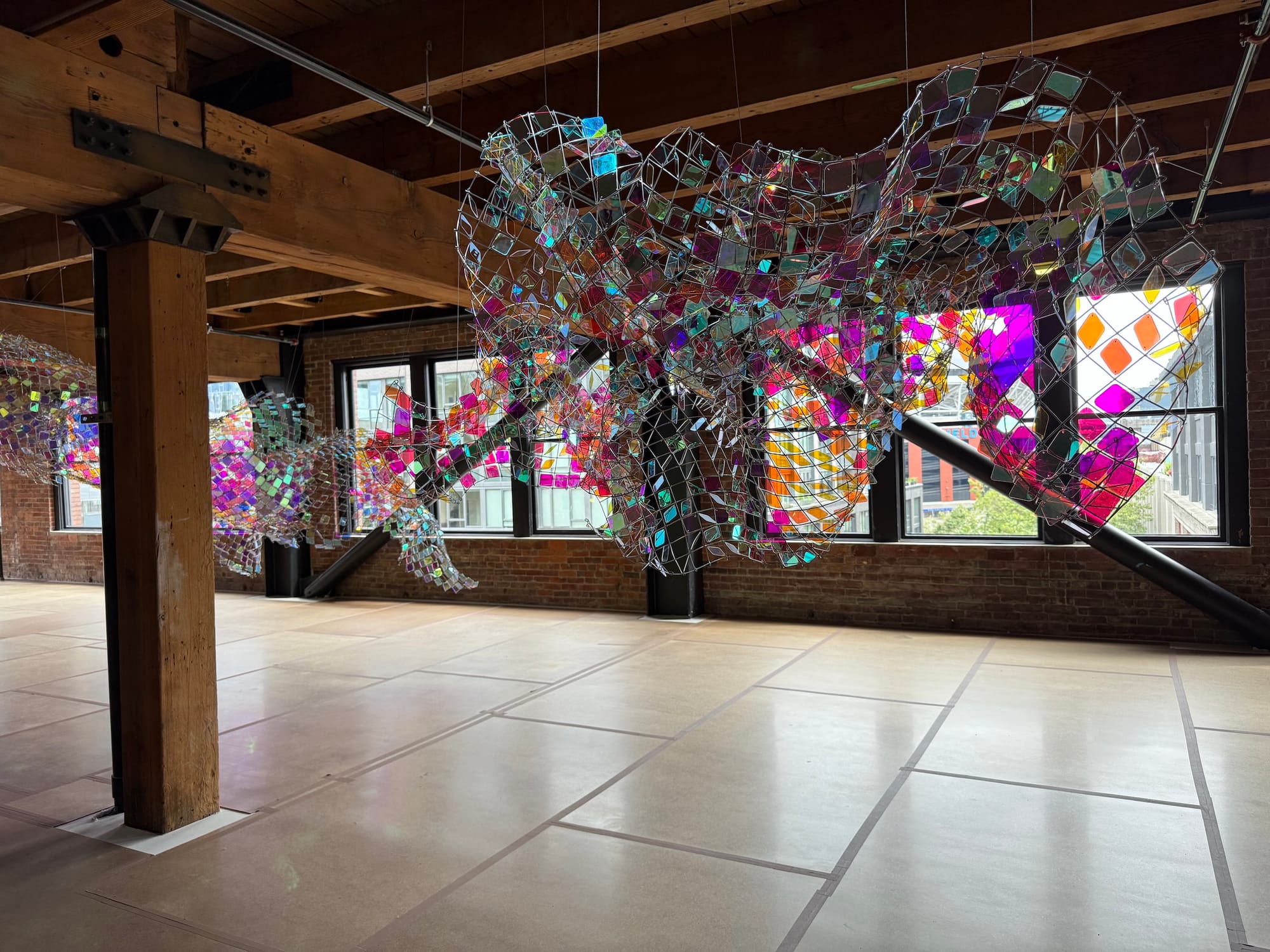 Photo of a brickwalled art gallery with an iridescent floating sculpture in front of windows
