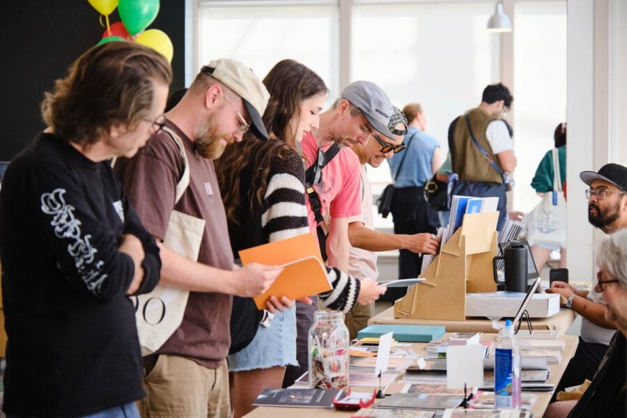 People browse a table covered in zines at a fair