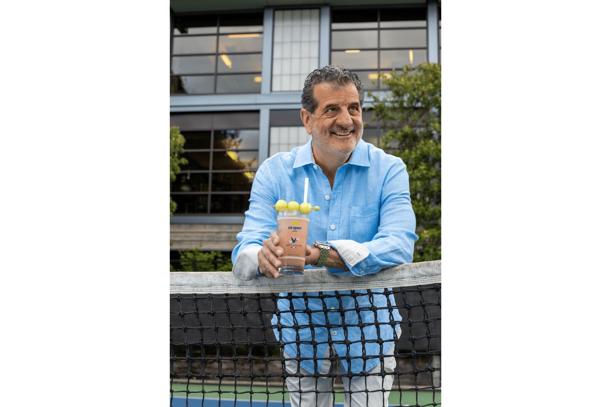 A person stands holding a cocktail in front of a tennis net