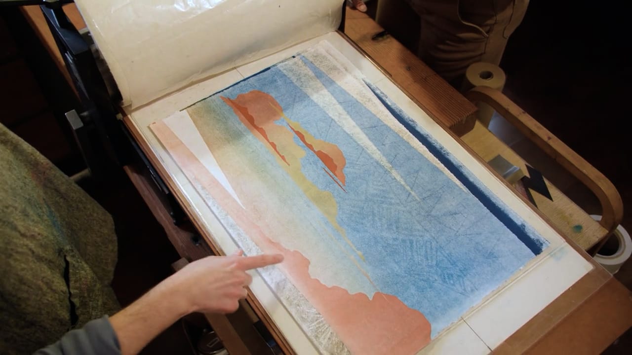 Photo of a person pointing at a print that looks like pink clouds on blue sky.