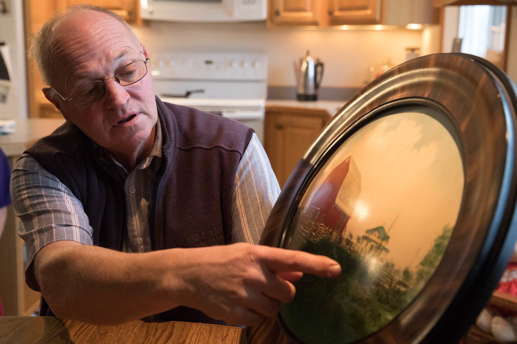 Owner Larry Stap of Twin Brook Creamery near Lynden, Washington sits at his dining room table, holding a painting of his farm as it was decades ago.