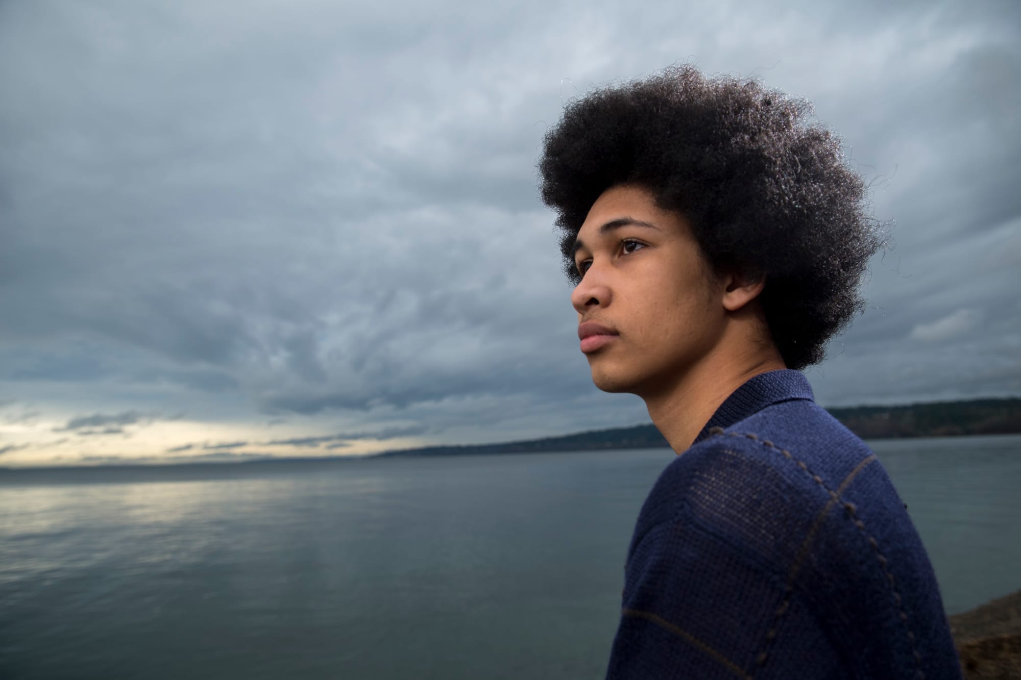 Plaintiff Aji Piper looks away from the camera in front of a body of water 