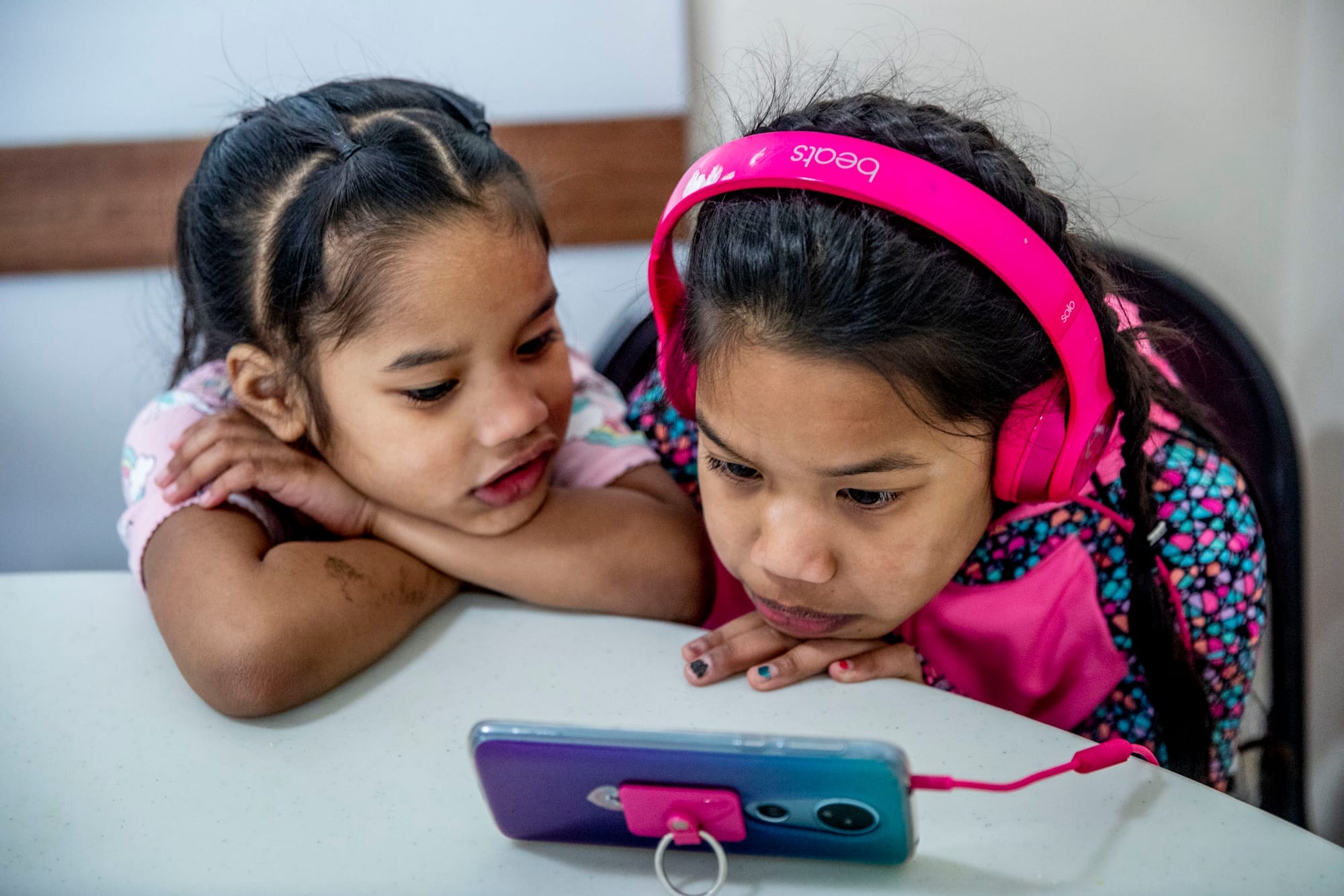 Sisters Faith, 4, left, and Zinnia Lejer, 7, watch cartoons on a phone in the common area at Mary's Place homeless shelter in Burien on March 1, 2019. (Photo by Dorothy Edwards/Crosscut)
