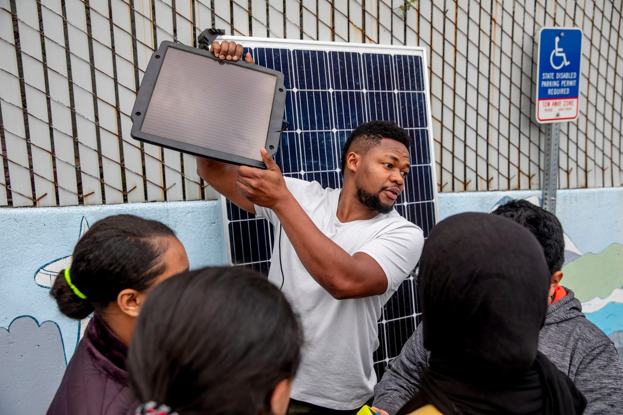 Edwin Wanji, center, teaches a group of kids from the Lake City Young Leaders program about how to work a solar panel at the Lake City Community Center on April 1. Wanji is the owner and founder of Sphere Solar Energy in Seattle and is often invited to talk to students about opportunities in solar. "I'm trying to create excitement around this field. It's renewable energy, it's exciting, there will always be more sunlight tomorrow," he says. "It's encouraging to see the kids' excitement about it." (Photo by Dorothy Edwards/Crosscut)