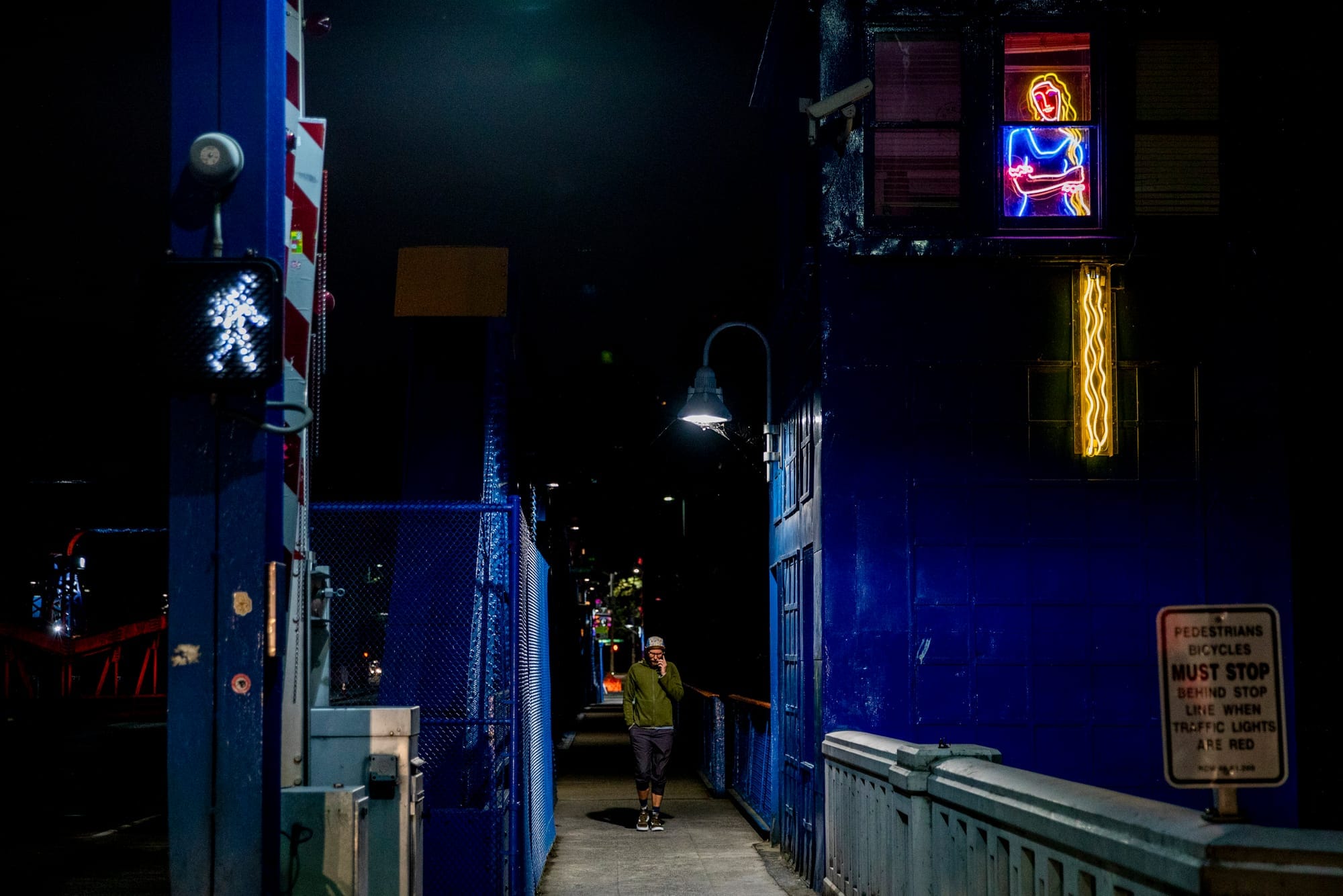 Man walks on bridge passed neon sign
