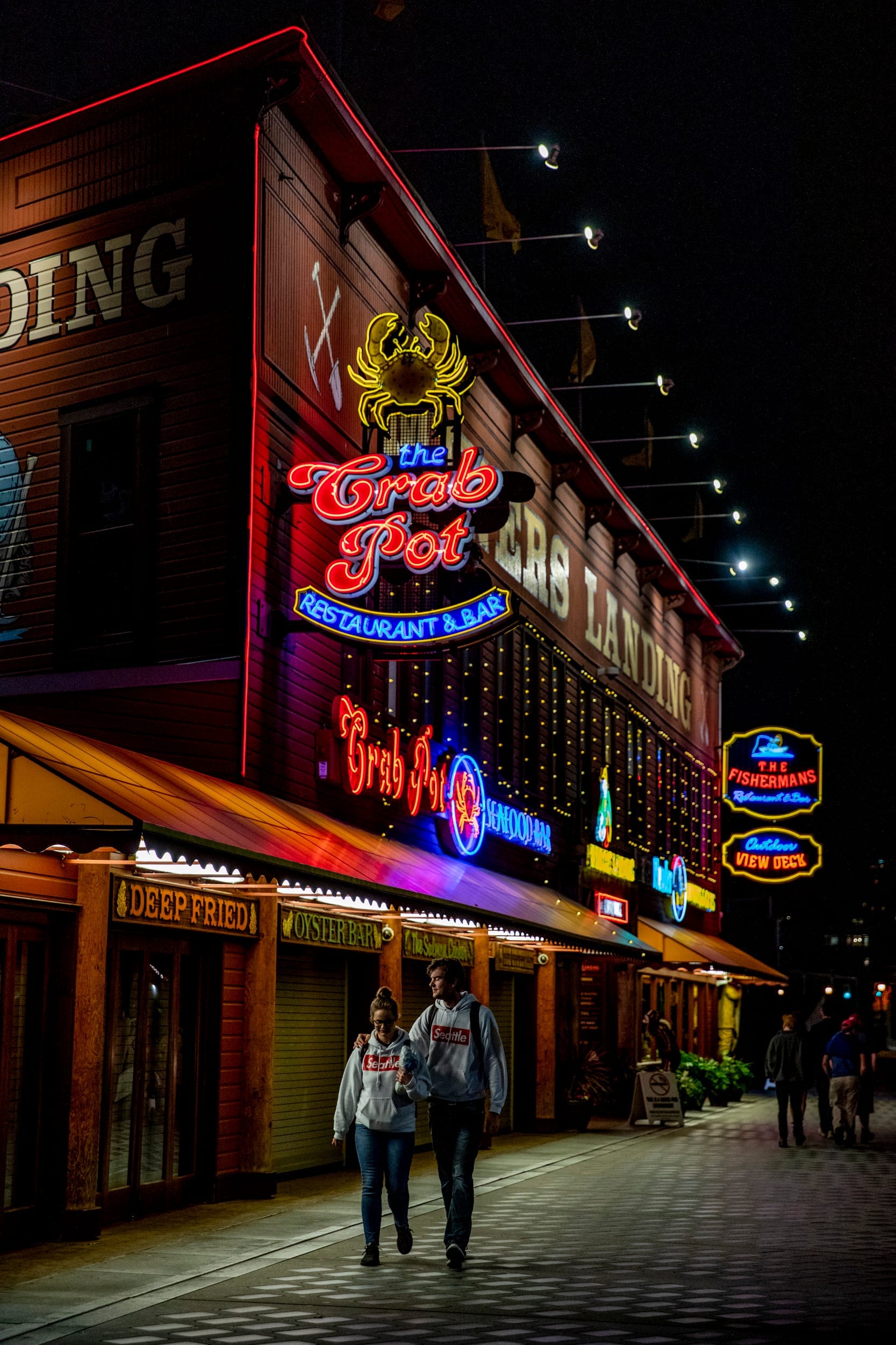 two people walk along the Seattle boardwalk at night