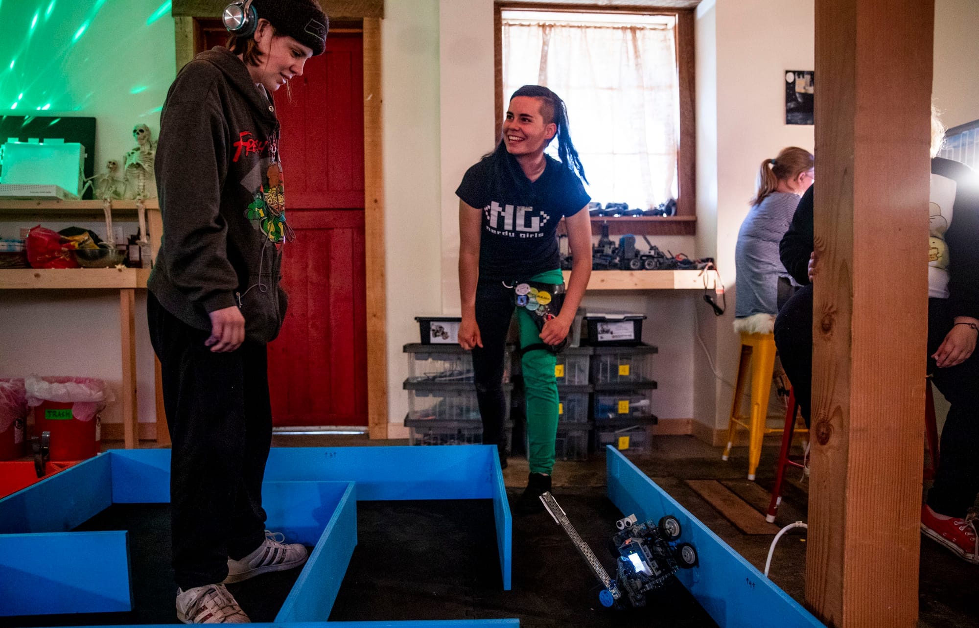 Nerdy Girls co-founder and high school senior Parker Mayer, right, encourages high school freshman Madison "Sparky" Sparks as she tests out her robot in a challenge course during a meetup in the Nerdy Girls barn in Ellensburg on May 17, 2019. (Photo by Dorothy Edwards/Crosscut)