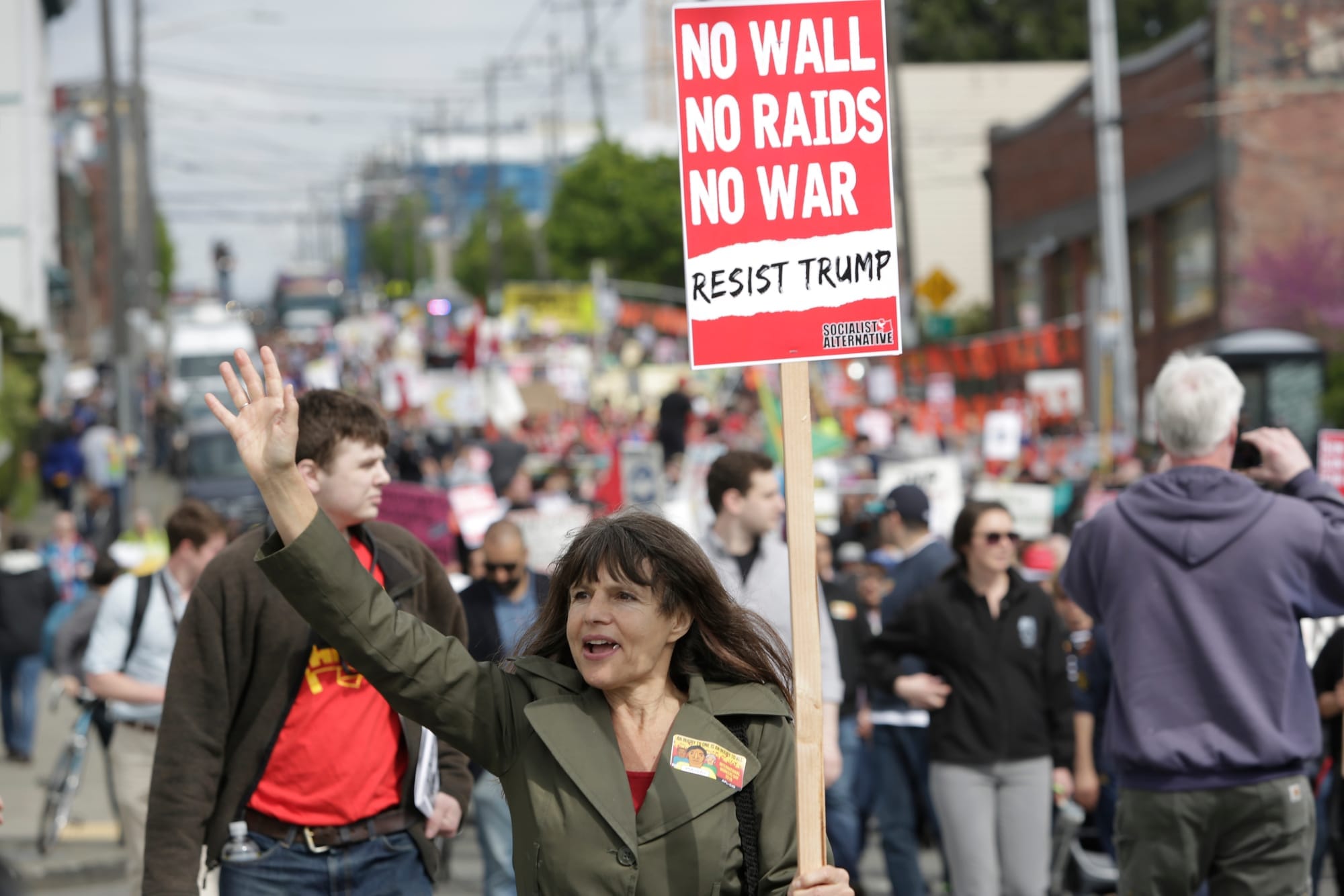 Preschool teacher Lauren Tozzi of Seattle, who says she never misses a march, waves to onlookers during the annual May Day March for Workers and Immigrant Rights in Seattle, May 1, 2018. (Jason Redmond for Crosscut)