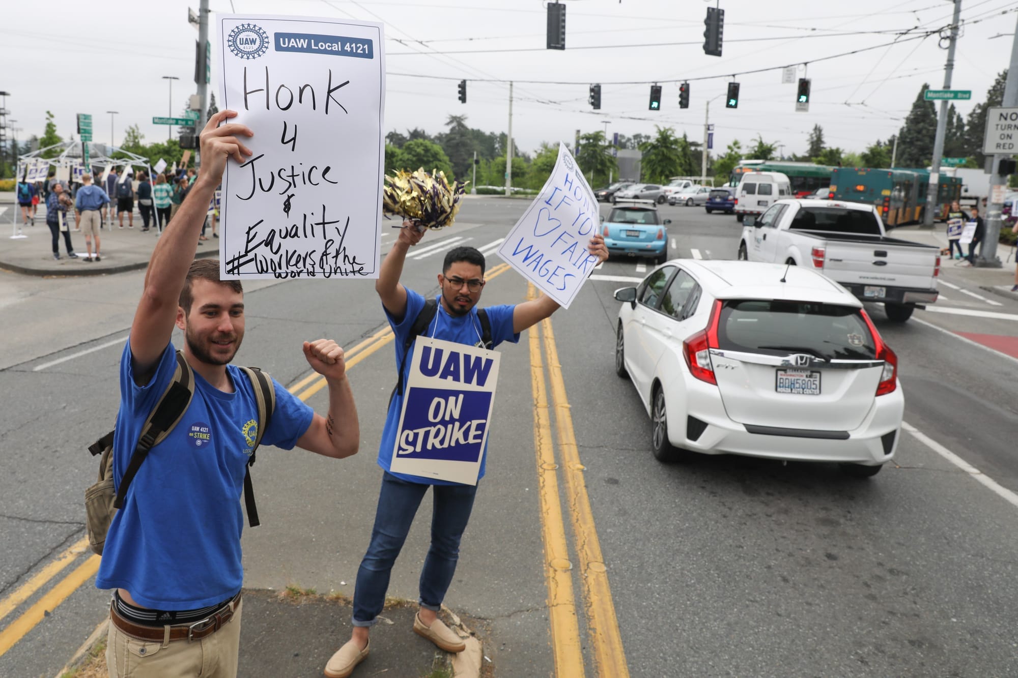 (From left) Mathieu Dubai and Yusri Supiyan, both students in political science at UW implore passing motorists along NE Pacific Street to honk in solidarity with them, during a one-day strike with graduate students who are represented by UAW Local 421 at the University of Washington in Seattle, May 14, 2018.