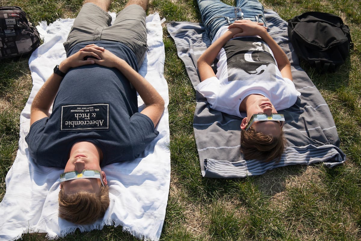 Two children look at the solar eclipse with their eclipse glasses on.