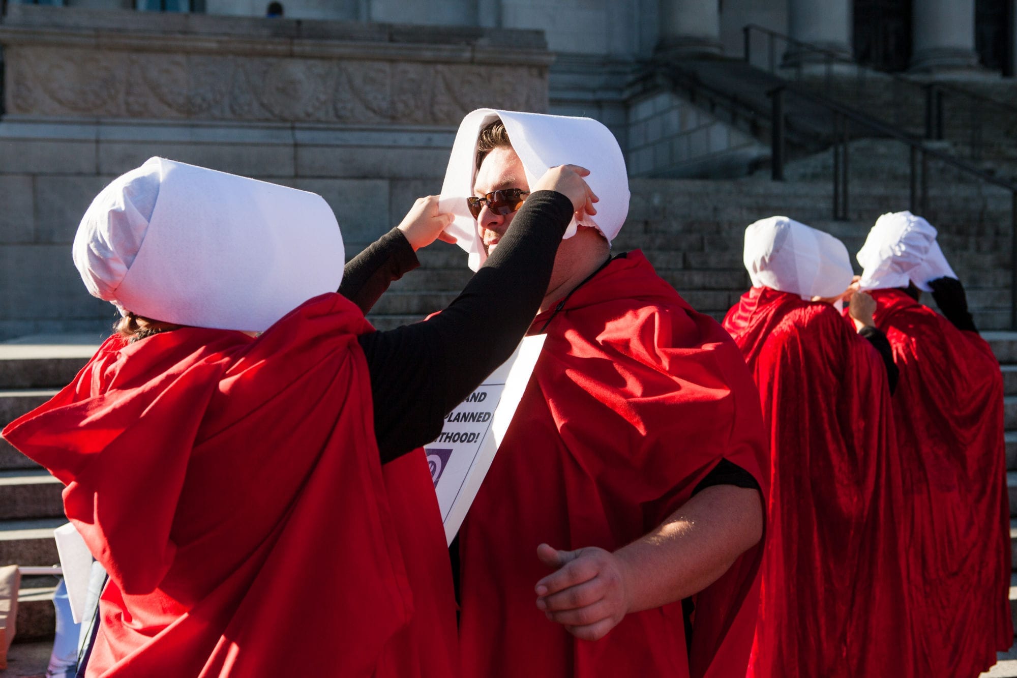 Shannon Spencer helps her roommate Dan McMahon into a red robe and bonnet.