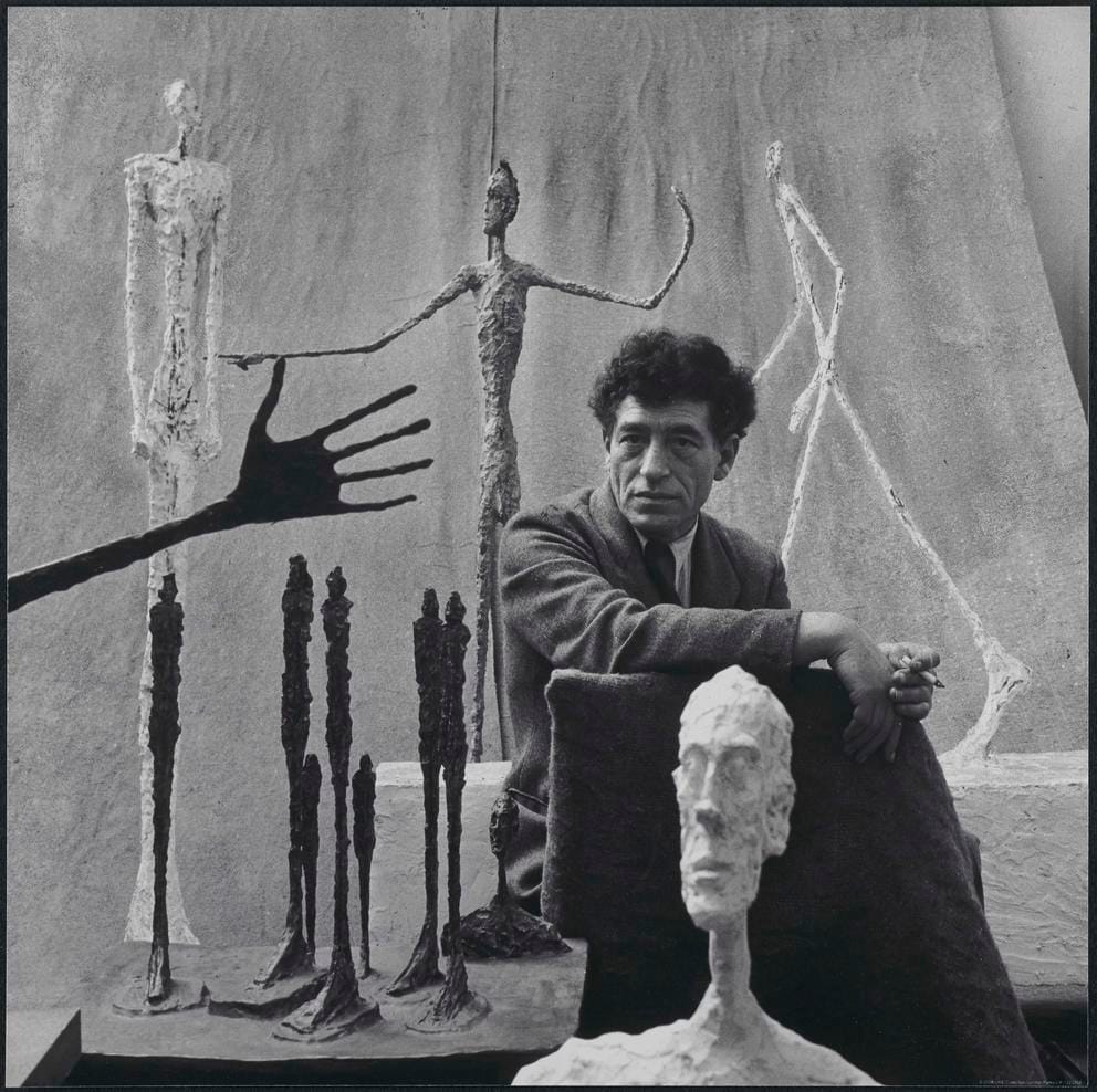 An artist in his studio, black and white photo featuring his slender artworks in metal and plaster