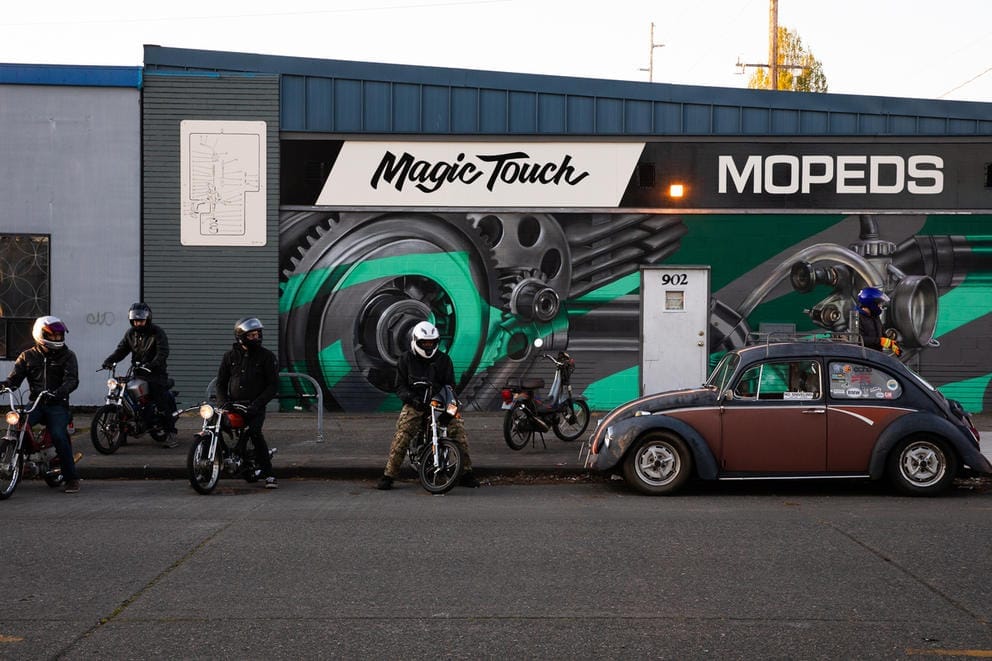 Mopeds and riders and a VW Bug car. 