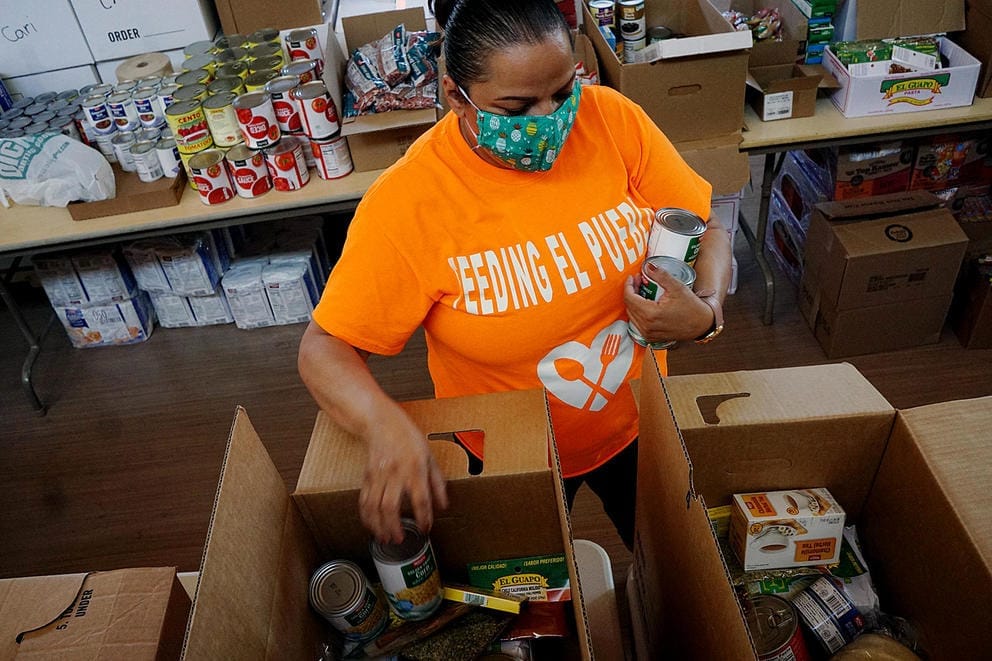 A person wearing a face mask packs food into a box
