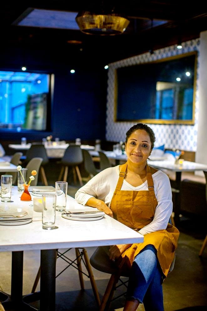 woman with apron sitting at table in empty restaurant, smiling at camera