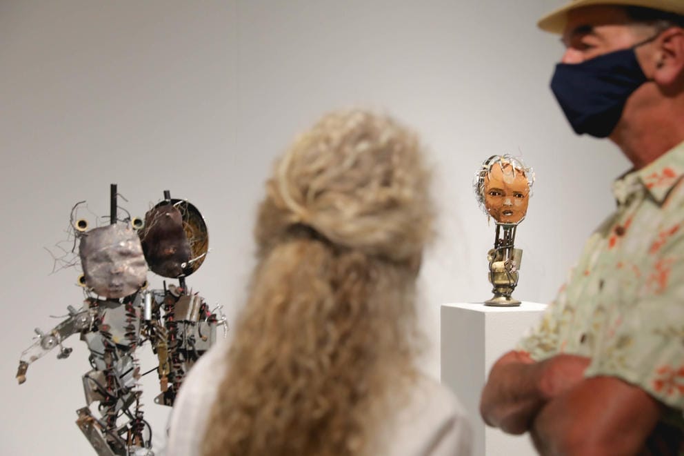 Two people photographed from the back and side, between them stand puppets made from recyled materials